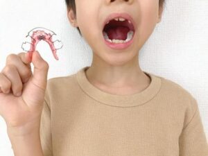 子どもが矯正器具をもって口を開けている様子